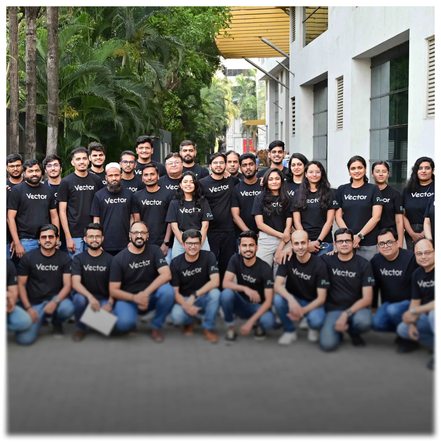 Group of young adults wearing matching black Vector t-shirts posing outdoors in front of trees and a white building