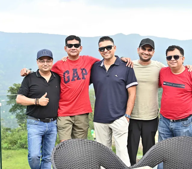 Five men standing outdoors with mountains in the background.