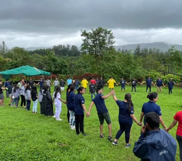 Group of people standing in a large circle holding hands on a grassy field.