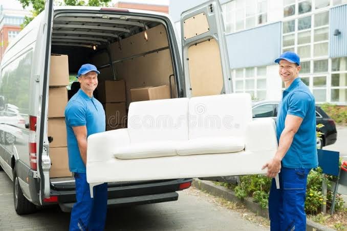 Two delivery crew members carrying a white sofa from a van